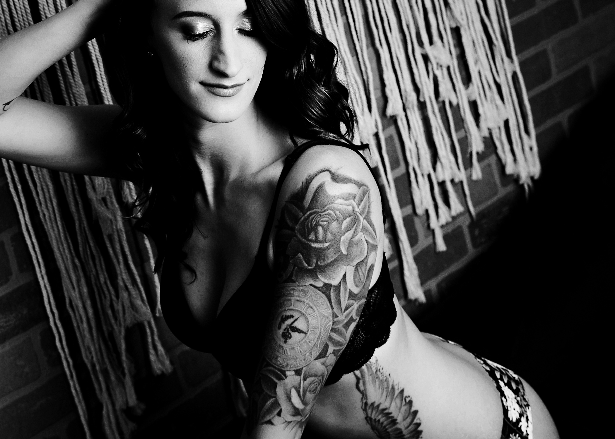 A woman in black lingerie runs a hand through her hair while standing by a brick wall after using madison yoga studios