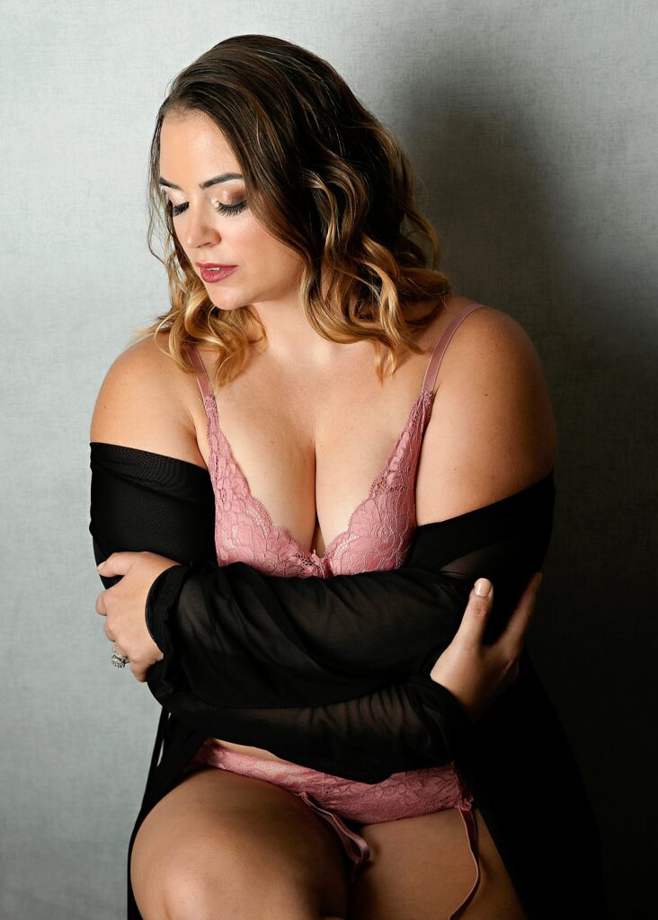 A woman in pink lace lingerie leans against a wall in a studio after getting some chicago microblading