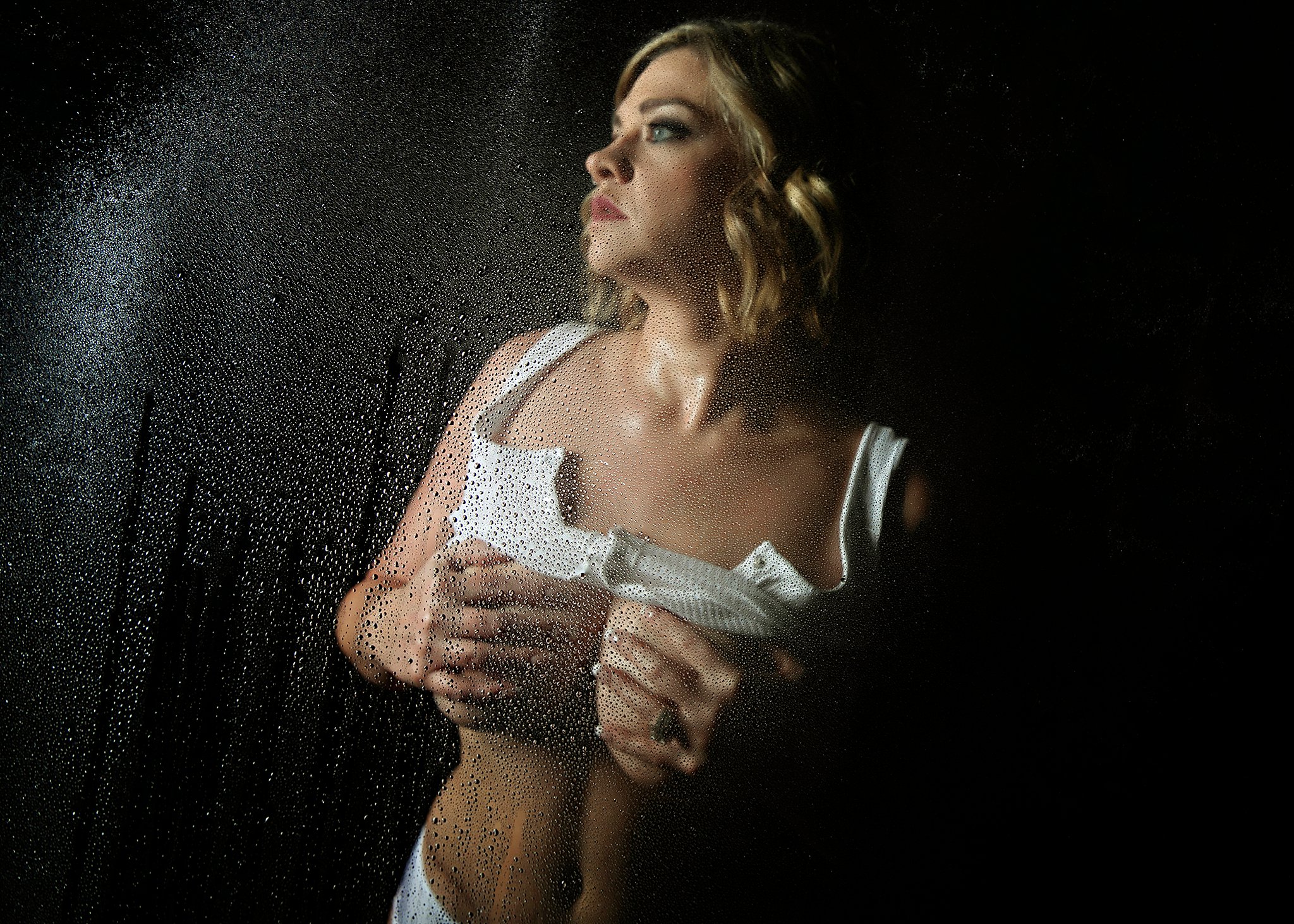 A woman covers her breast while standing in a window in white lingerie during a boudoir session for her milwaukee bachelorette party