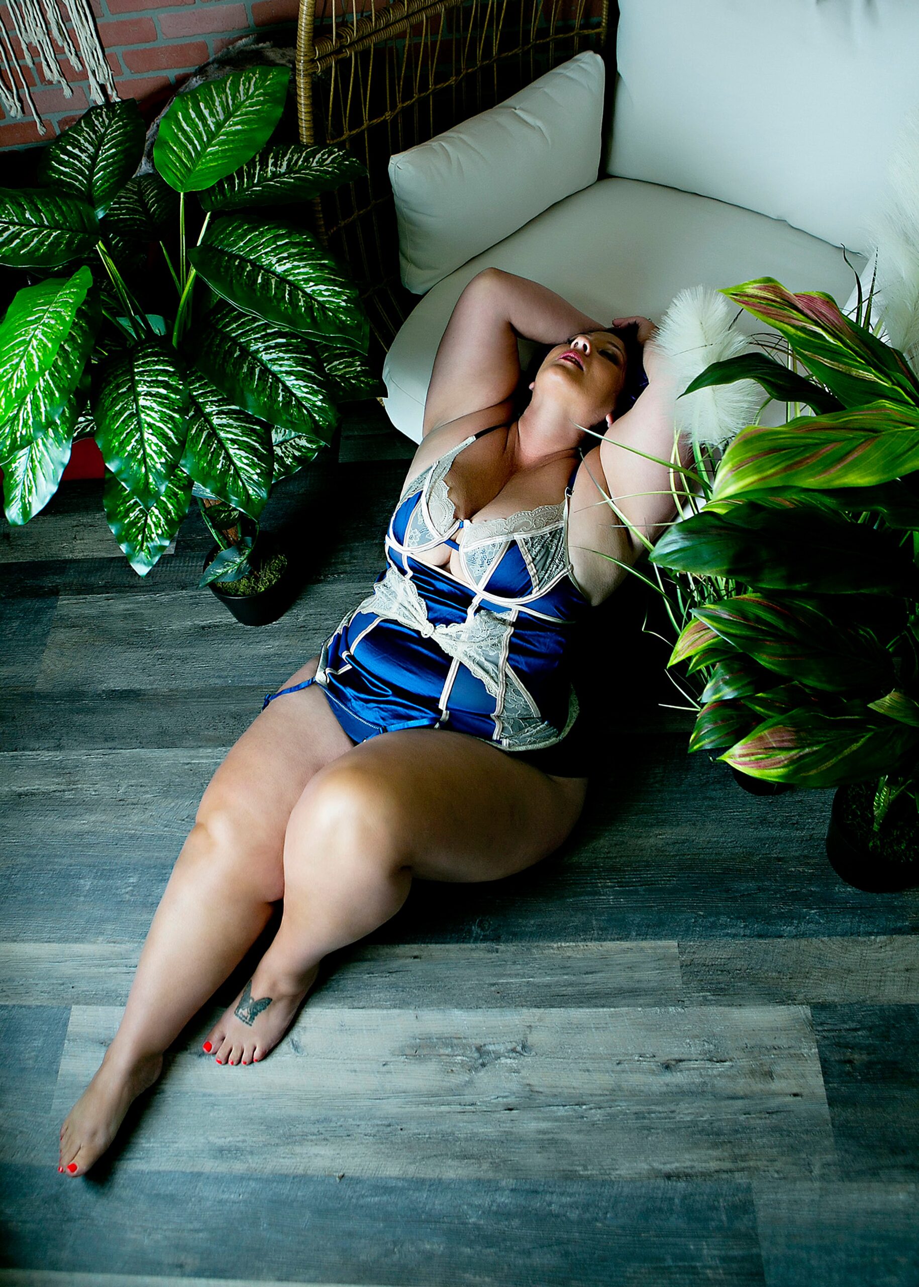 A woman in blue lingerie sits on the floor while leaning back onto a white chair in a studio after some sugaring madison wi